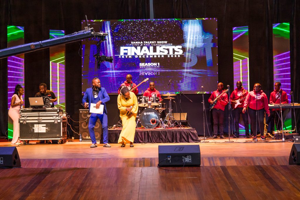 Event hosts in vibrant blue and yellow outfits interacting with the band and audience on the main stage.