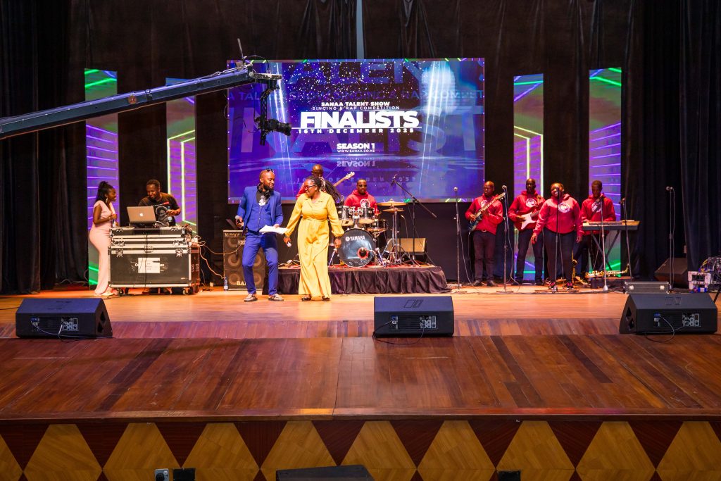 Event hosts in vibrant blue and yellow outfits interacting with the band and audience on the main stage.