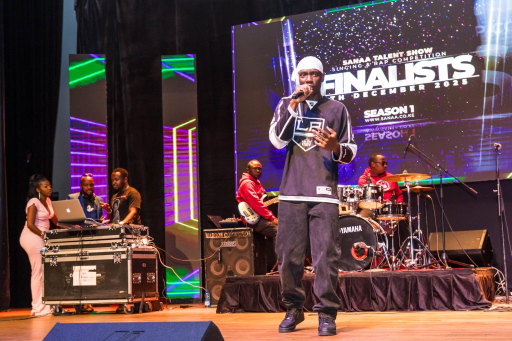 A male performer in a jersey and durag rapping on stage while the house band plays in the background.