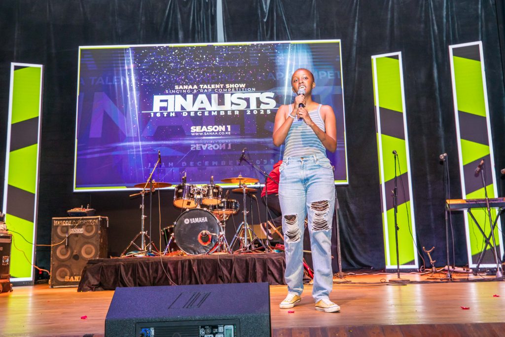 A young female singer in a striped top and distressed jeans performing with a microphone on a professional stage.