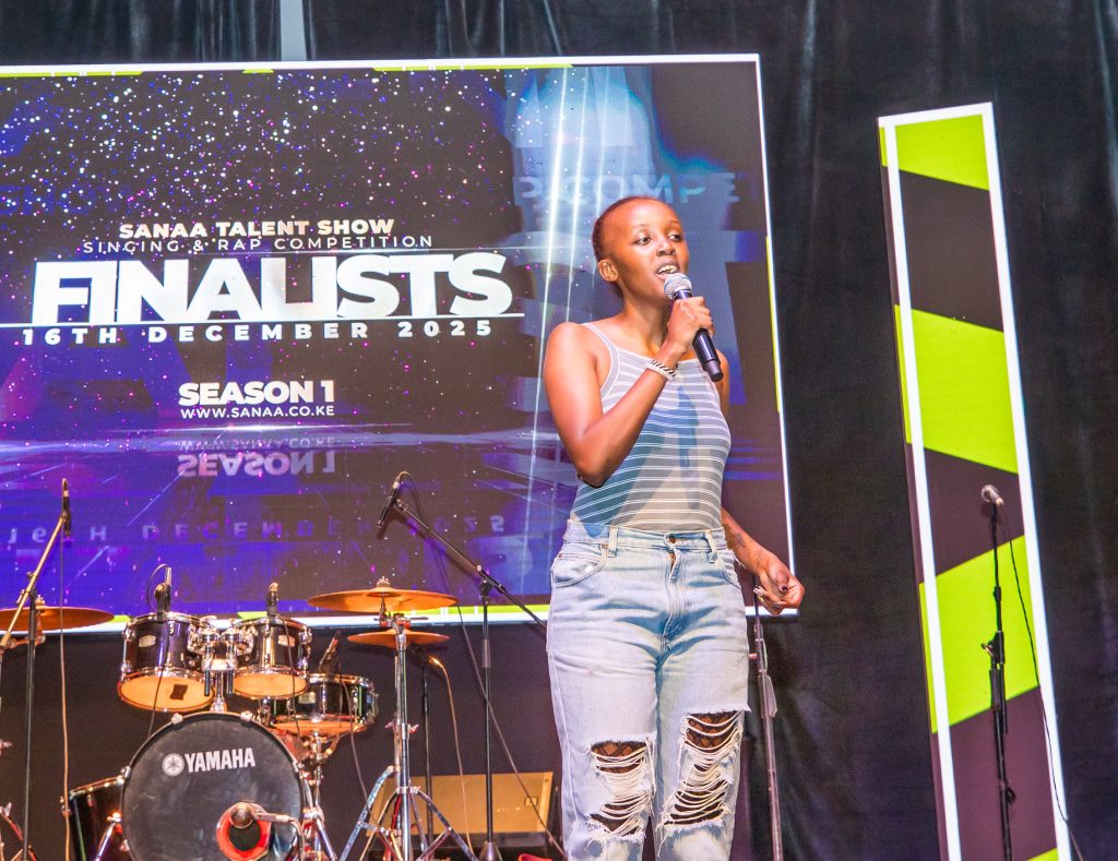 A young female singer in a striped top and distressed jeans performing with a microphone on a professional stage.