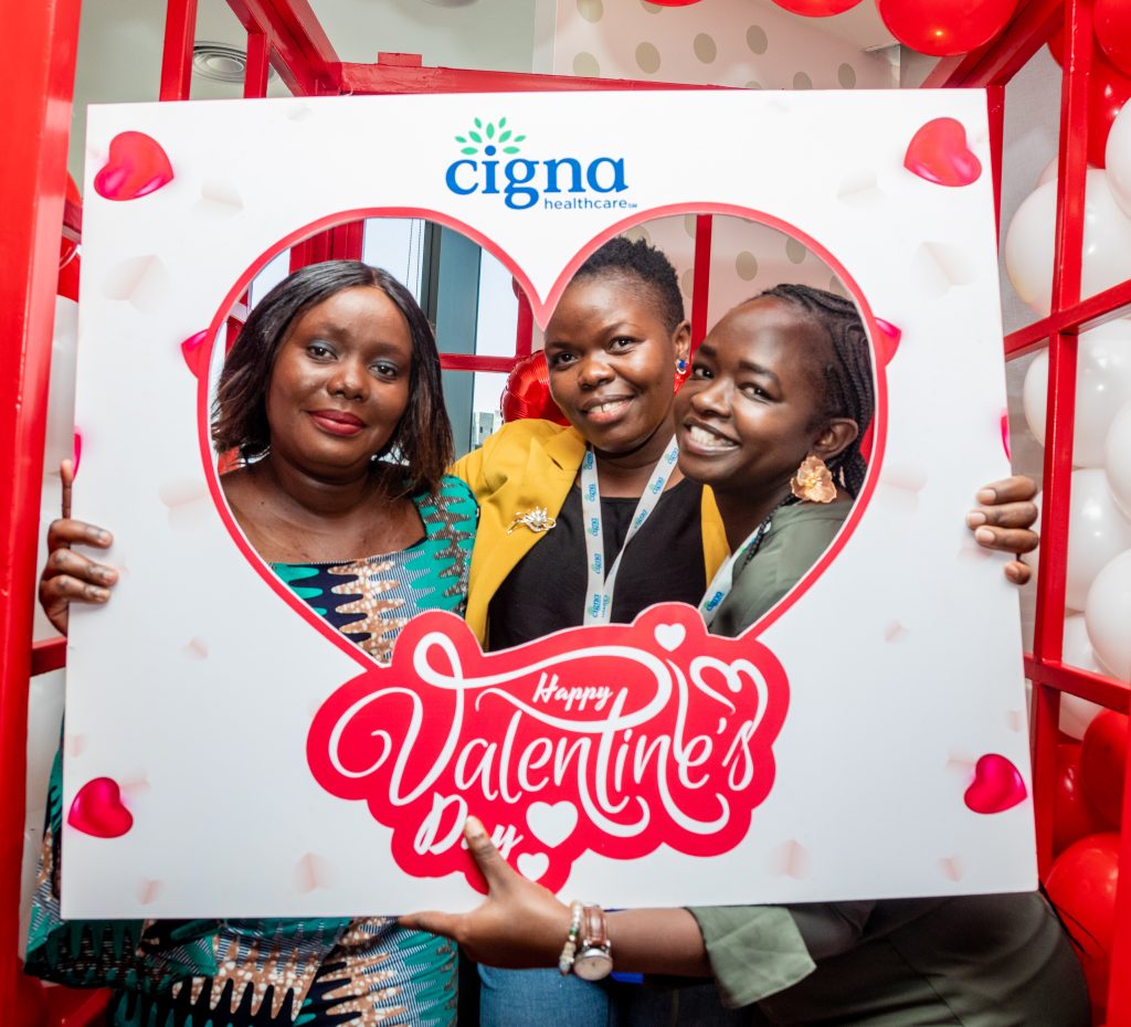 Three women holding a Cigna Healthcare Valentine's Day photo frame, smiling brightly at a corporate event.