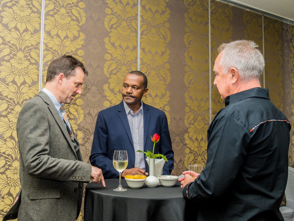 Three businessmen networking and talking around a cocktail table during a JBQ Africa event, photography by Mintglint Media Nairobi.
