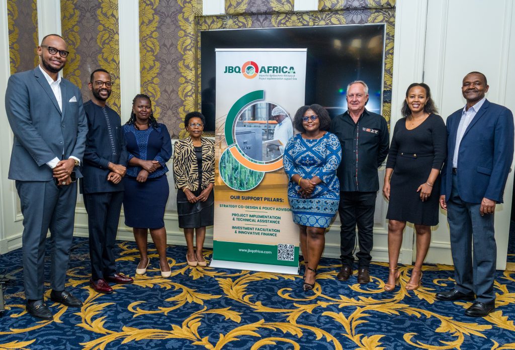 A group of eight professionals posing happily in front of the JBQ Africa banner at a corporate networking event in Nairobi.