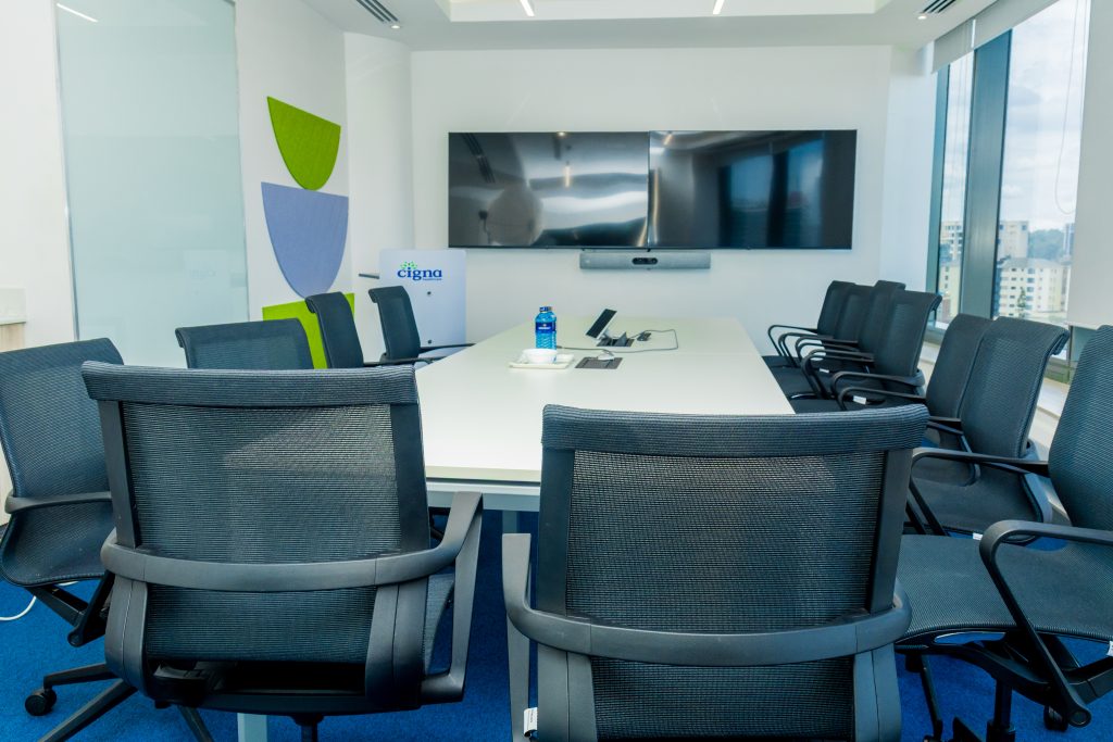 An empty, well-lit modern corporate boardroom with a long table, black mesh chairs, screens, and a Cigna podium
