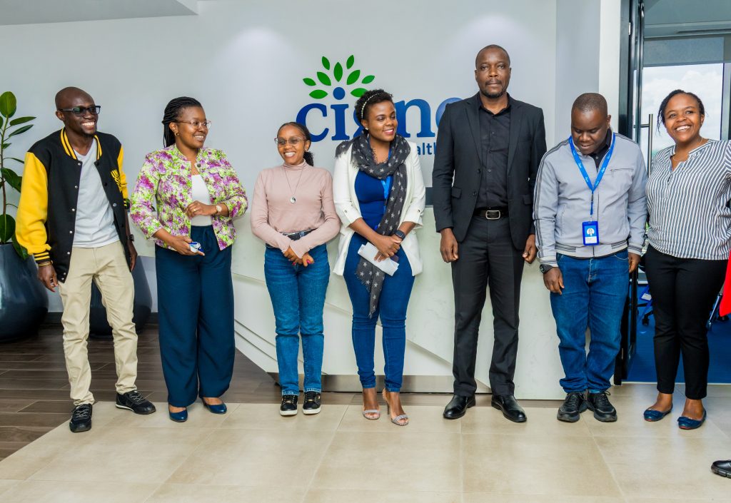 A diverse group of seven professionals standing together and smiling in front of the Cigna Healthcare reception sign in Nairobi.