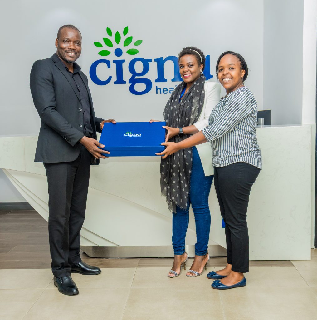 A man in a black suit handing a blue Cigna gift box to two smiling women at the Cigna Healthcare reception, shot by Mintglint Media.