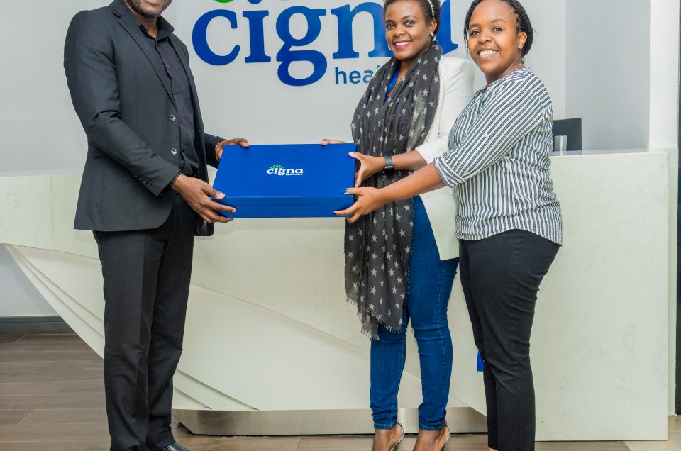 A man in a black suit handing a blue Cigna gift box to two smiling women at the Cigna Healthcare reception, shot by Mintglint Media.