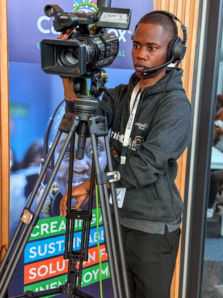 A close-up of a focused Mint Glint Media camera operator manning a professional Sony video camera on a carbon-fiber tripod. He is wearing a communication headset and a hoodie with the Mint Glint Media logo.