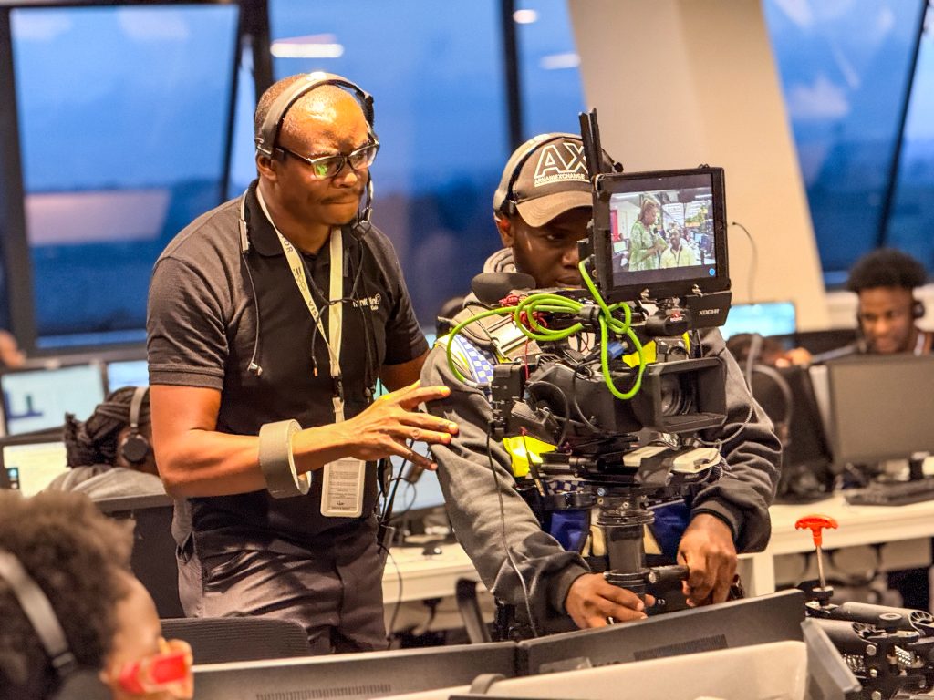 Close-up of two Mint Glint Media crew members working closely together in an office. One operates a heavy professional camera rig while the other, wearing glasses and a headset, guides the operator to ensure a smooth shot.