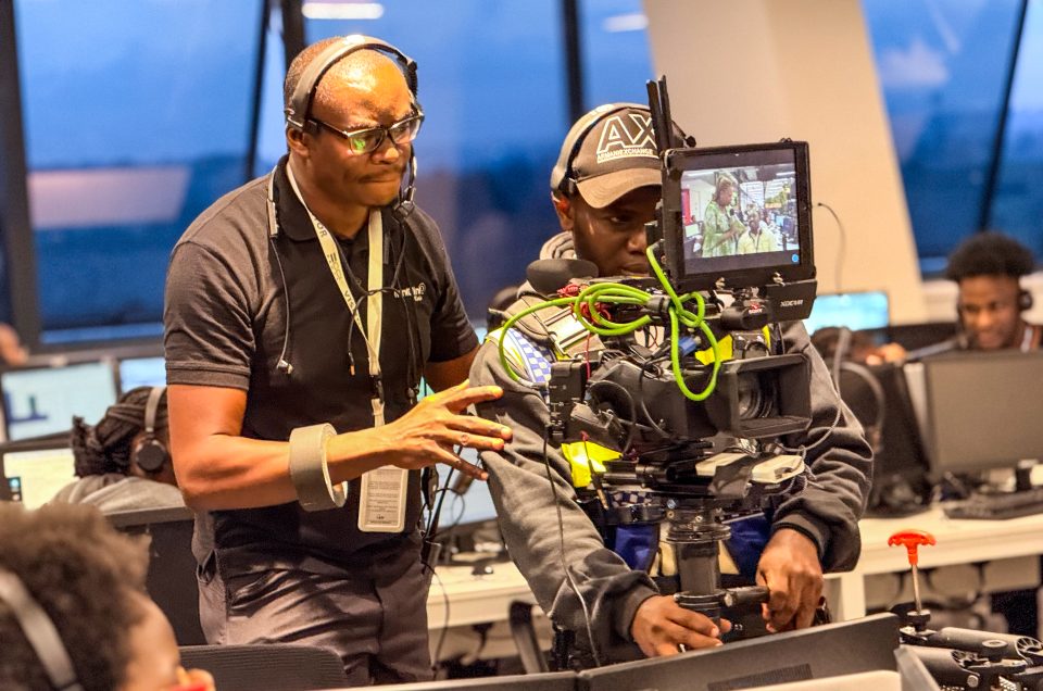 Close-up of two Mint Glint Media crew members working closely together in an office. One operates a heavy professional camera rig while the other, wearing glasses and a headset, guides the operator to ensure a smooth shot.